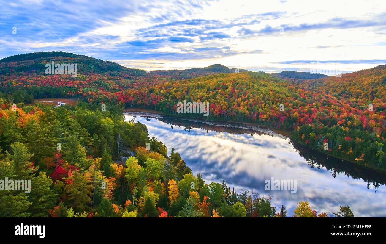 Aerial over stunning pond reflection blue sky and clouds and surrounded by mountains of fall foliage in morning light Stock Photo