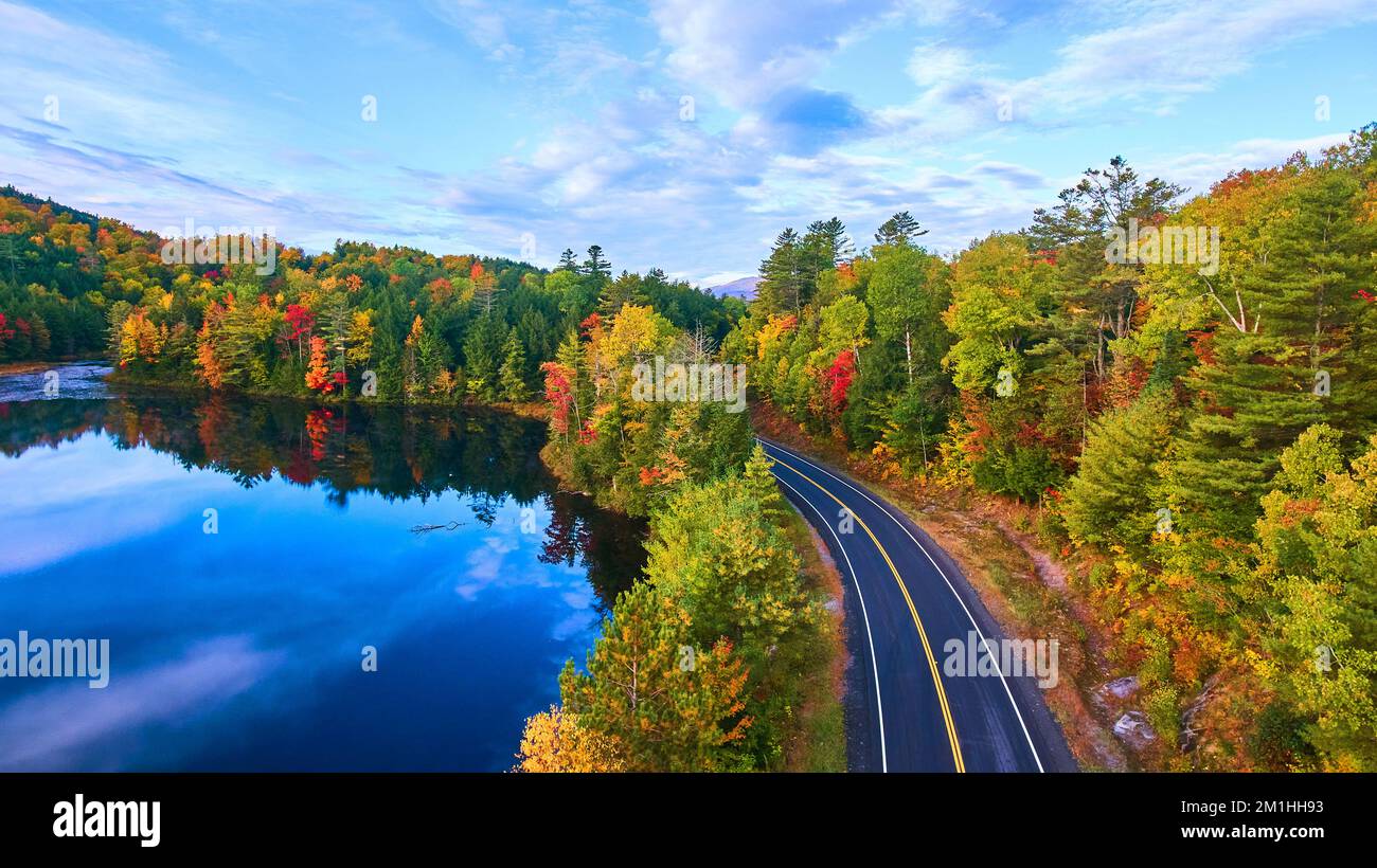 Aerial over road next to blue lake and surrounded by fall forest Stock Photo
