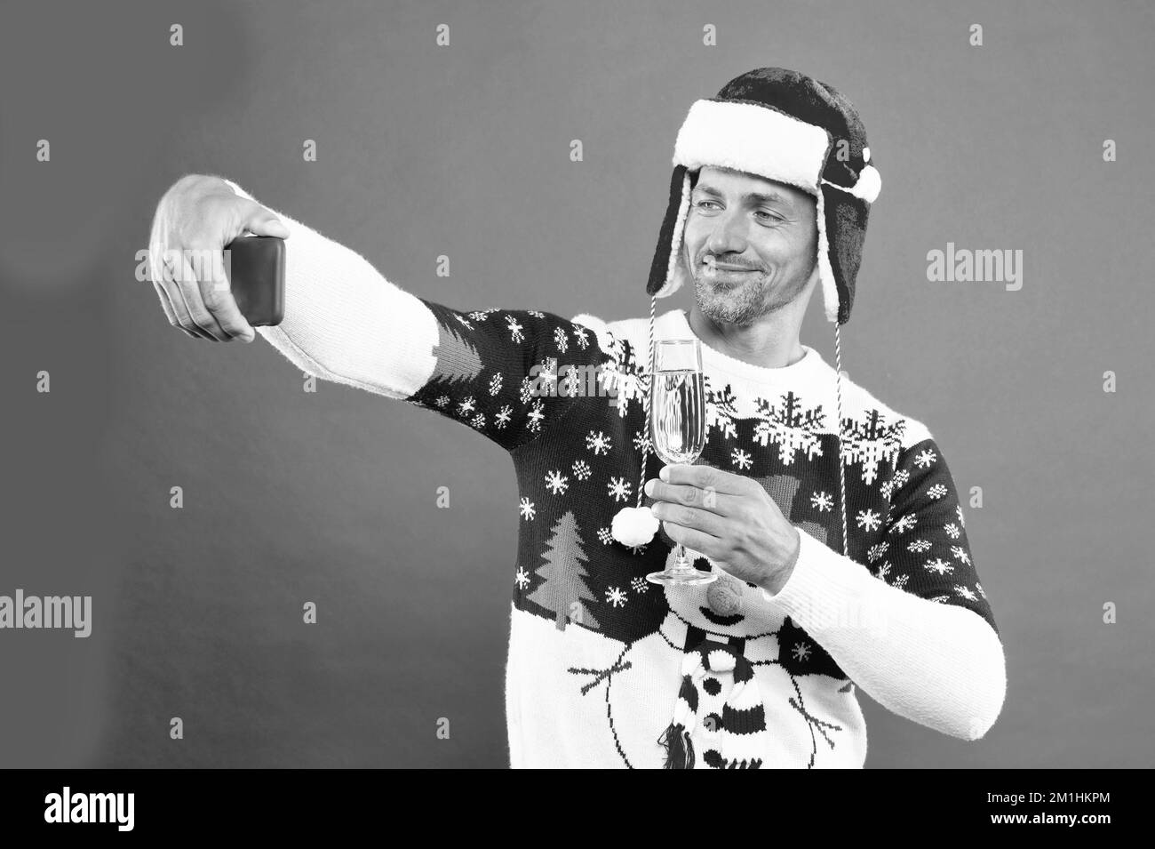 positive man in winter sweater and hat making selfie on smartphone while drinking champagne, xmas. Stock Photo