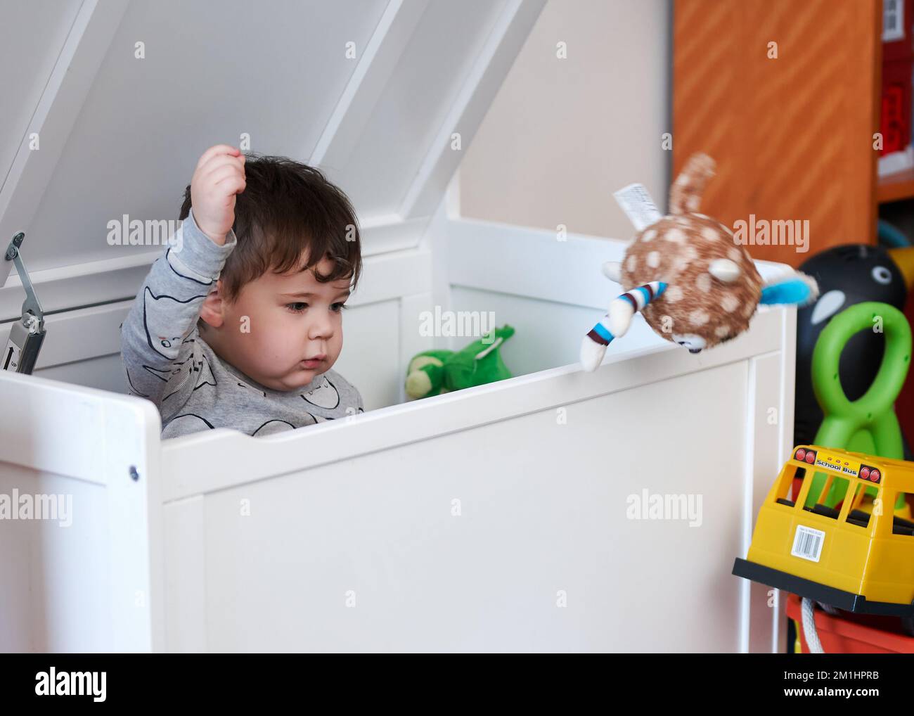 cute little boy throwing toys out of the toy box while sitting inside