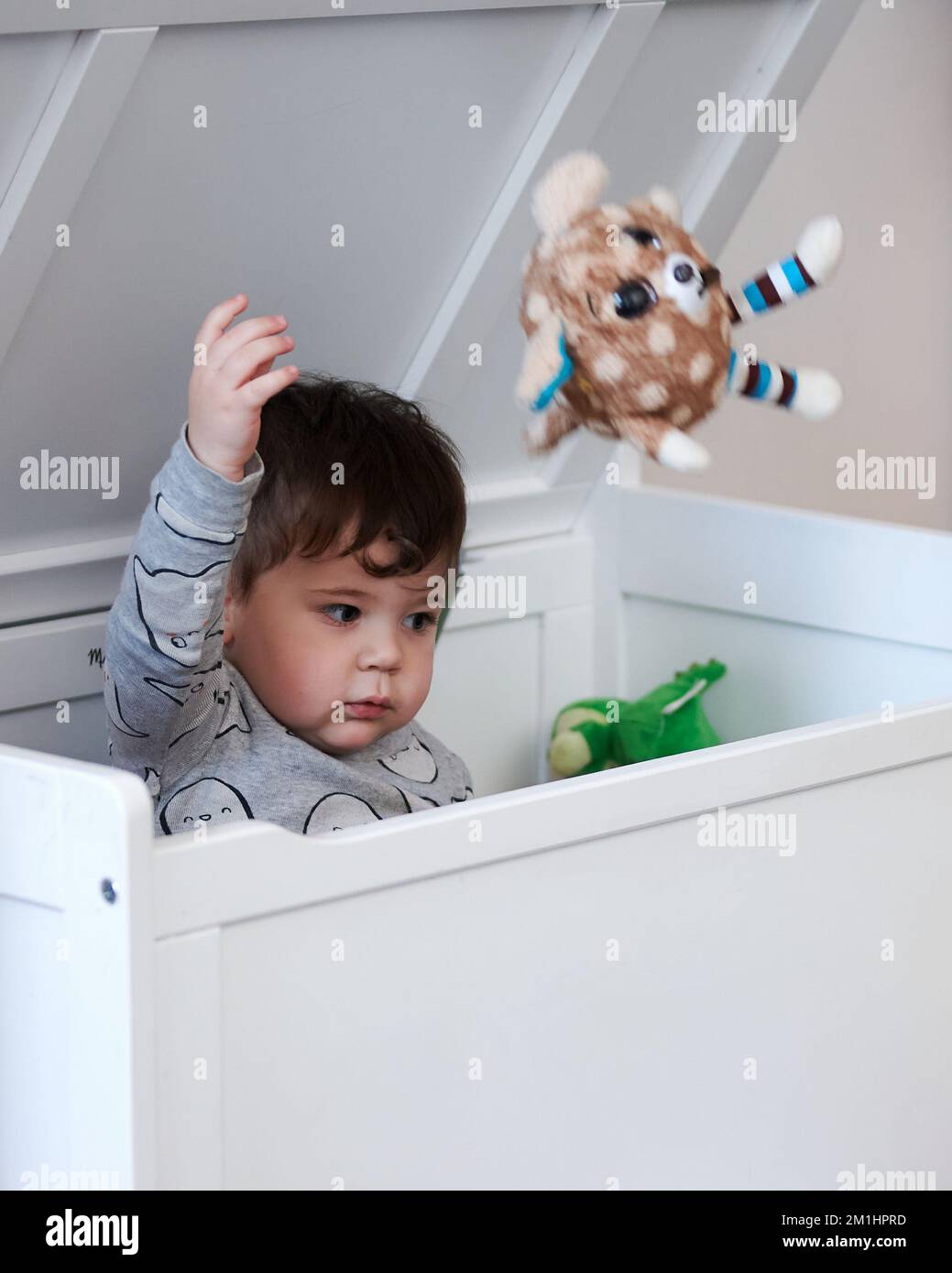 cute little boy throwing toys out of the toy box while sitting inside