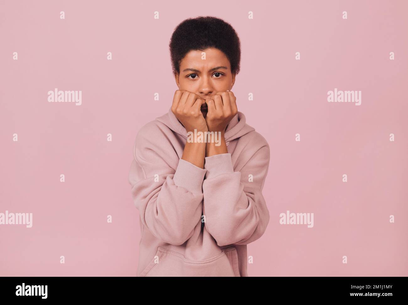 Nervous black young woman biting her nails. Frustrated beautiful african american girl in casual clothes feeling anxious and worries. Studio portrait. Stock Photo