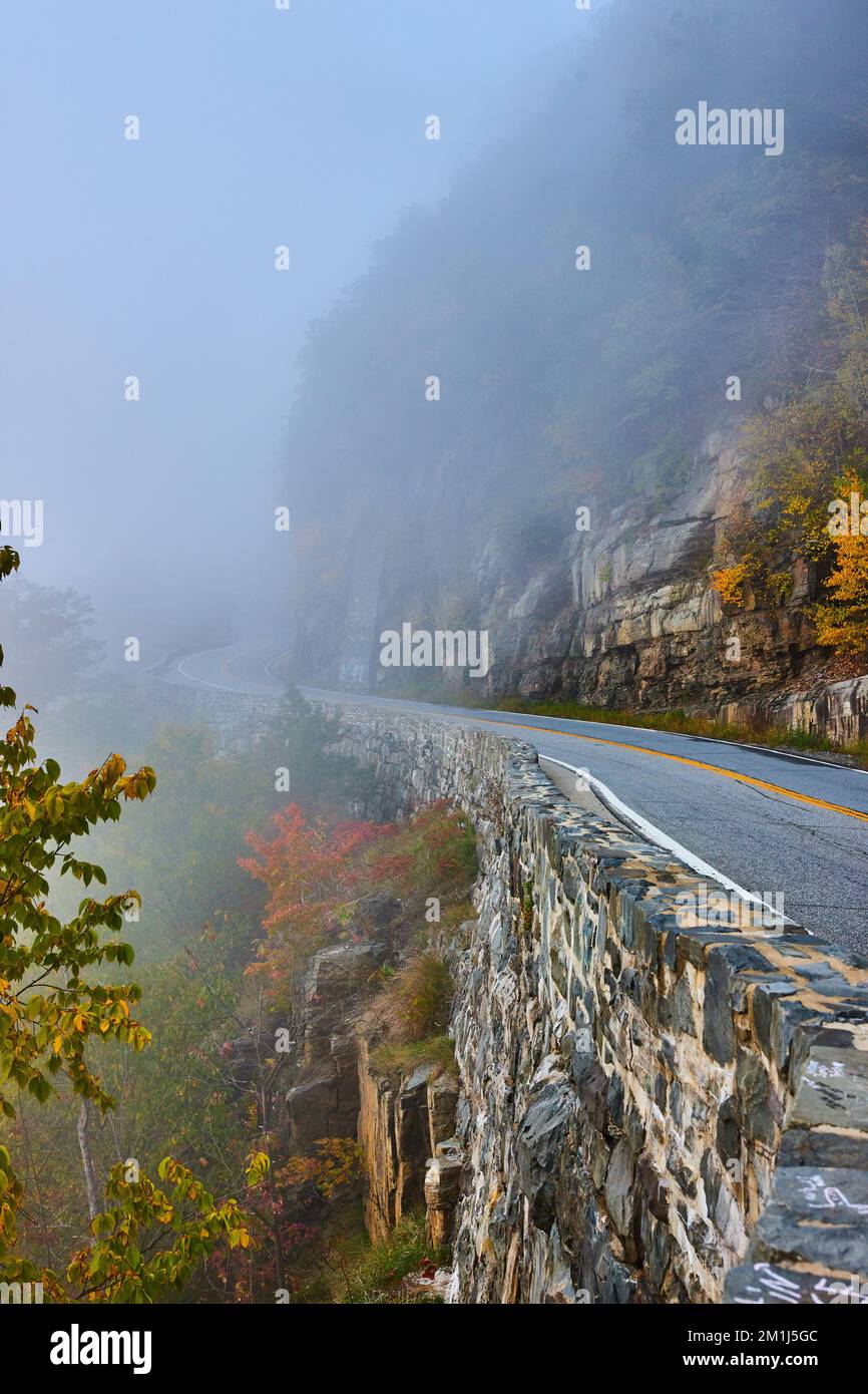 Foggy morning on road through cliffs next to stone block wall Stock Photo