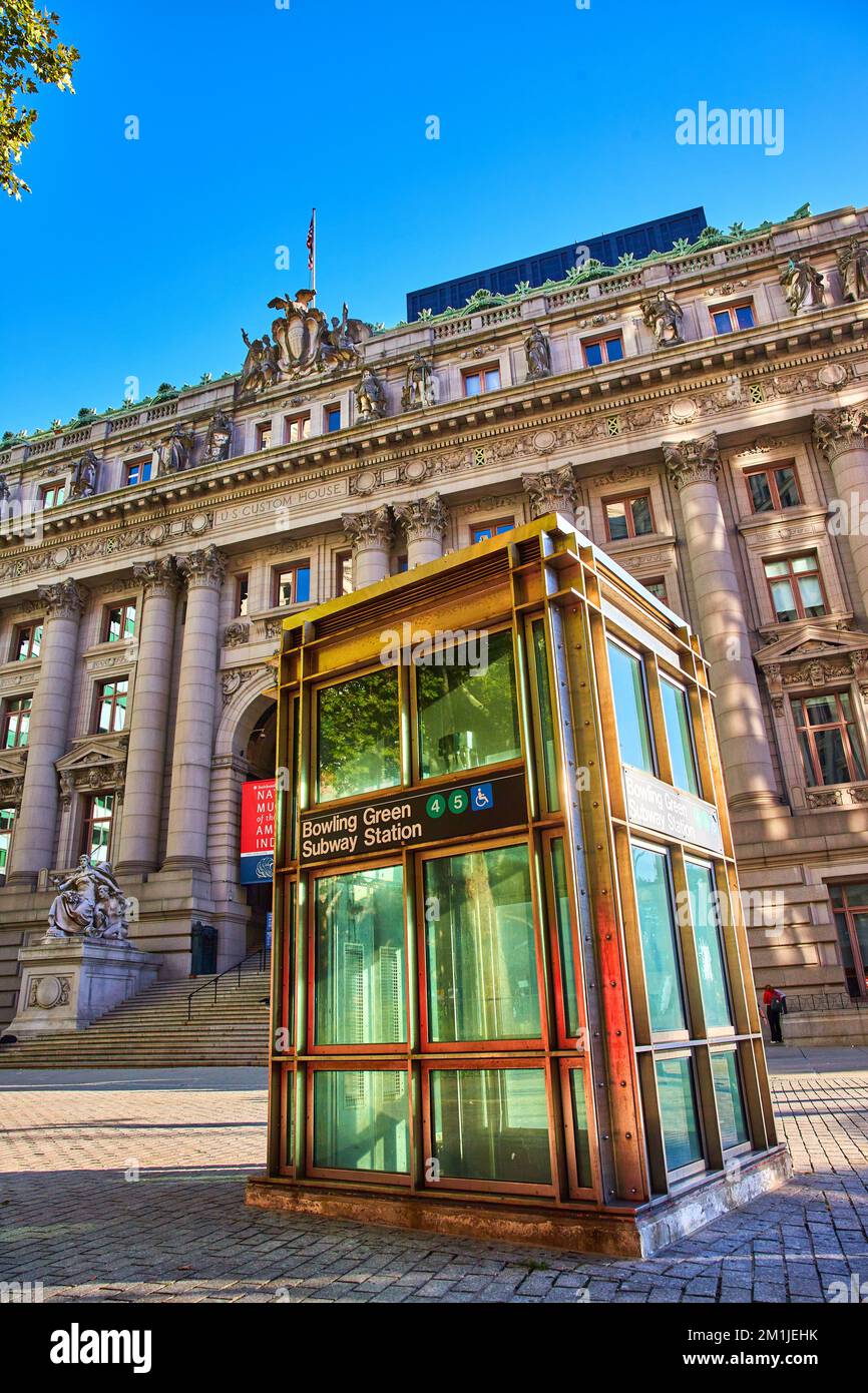 Light shines on small Bowling Green subway entrance in New York City streets outside of huge limestone museum building Stock Photo