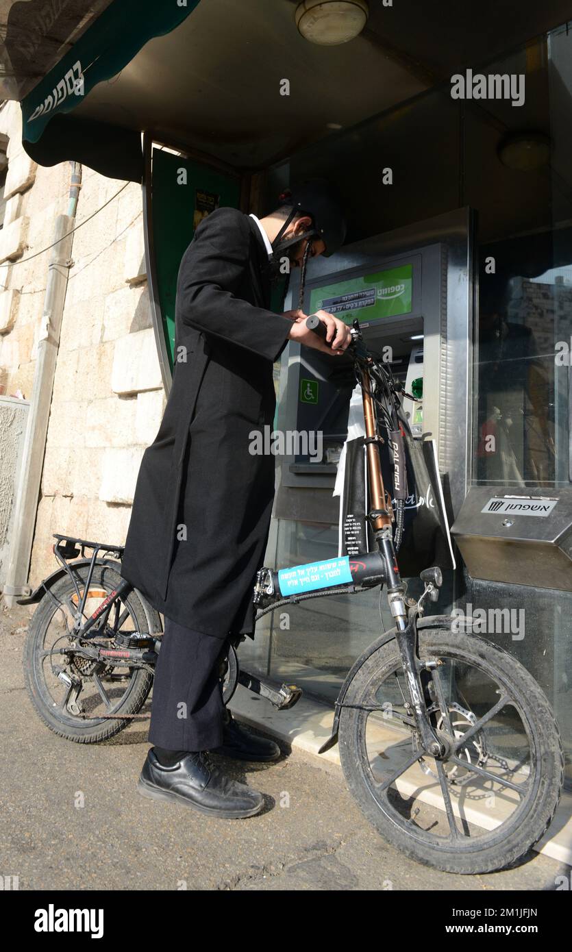A Haredi Jewish man stopping at the ATM with his bicycle. Stock Photo