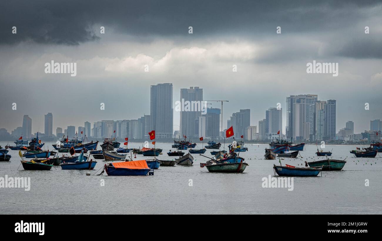 Traditional Vietnamese wooden fishing boats moored off My Khe beach across the bay from the modern sea front at Danang, Vietnam. Stock Photo