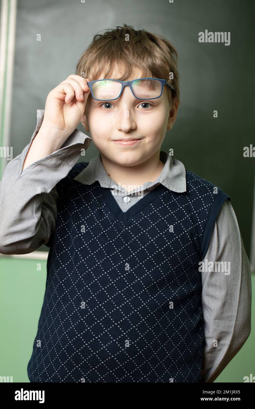 Portrait of a funny schoolboy in glasses at the blackboard. Ten year