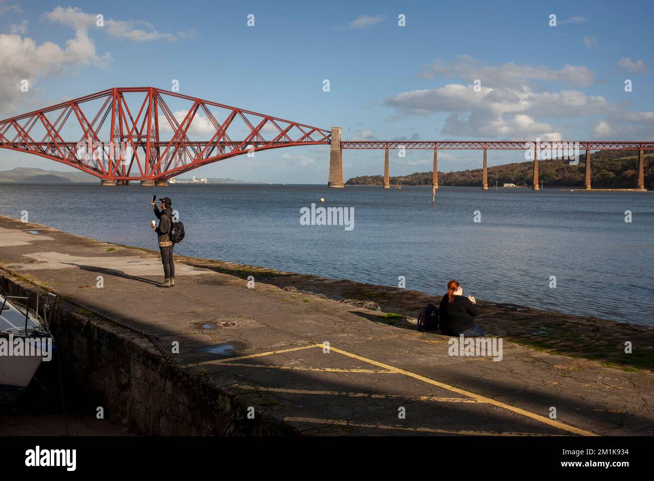 People stand on the quayside in South Queensferry with the Forth rail bridge in the background, West Lothian, Scotland UK 2022 Stock Photo