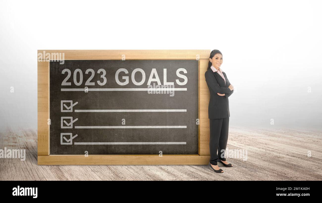 Asian businesswoman standing with the 2023 goal list is on the little blackboard. Goals of 2023