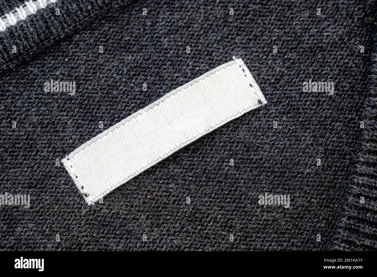 White blank label, patch or tag with space for text  on knitted gray sweater, top view Stock Photo