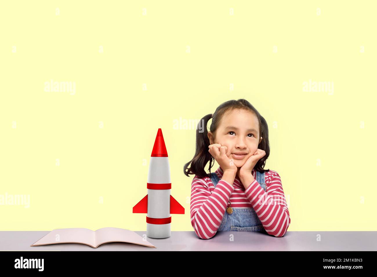 Asian little girl dreaming about flying a rocket on a colored background. National Science Day Stock Photo
