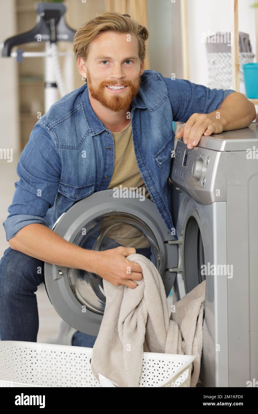 young man loading clothes into washing machine in kitchen Stock Photo