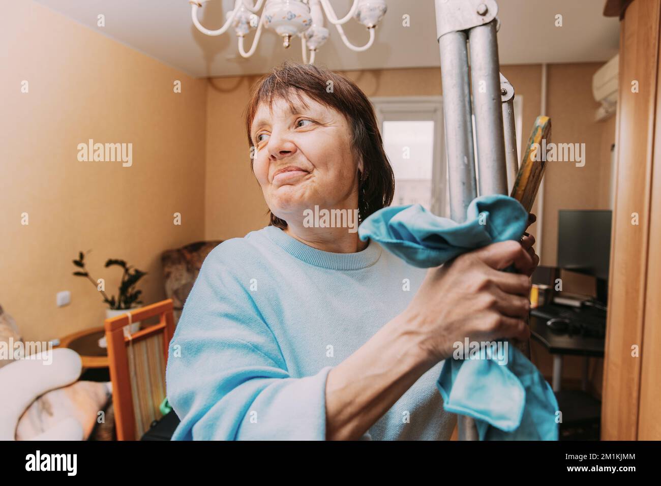 Happy Shy Mature Woman Cleaning Apartment. Concept Of Household And People In Retirement. Elderly Woman Cleaning Apartment. Active Seniors Concept Stock Photo