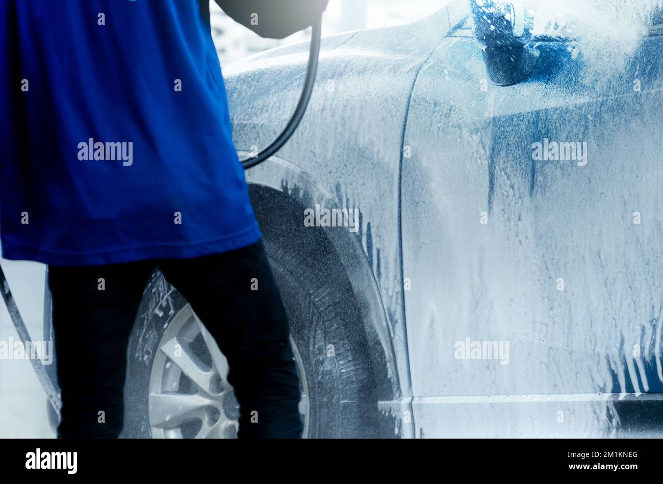 Worker washes blue SUV car with soap foam. Exterior carwash. Car care business. Vehicle cleaning