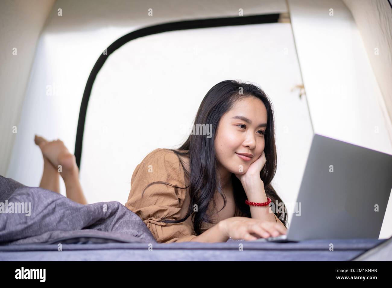 Young Asian woman using computer laptop while vacation in the tent at summer time Stock Photo