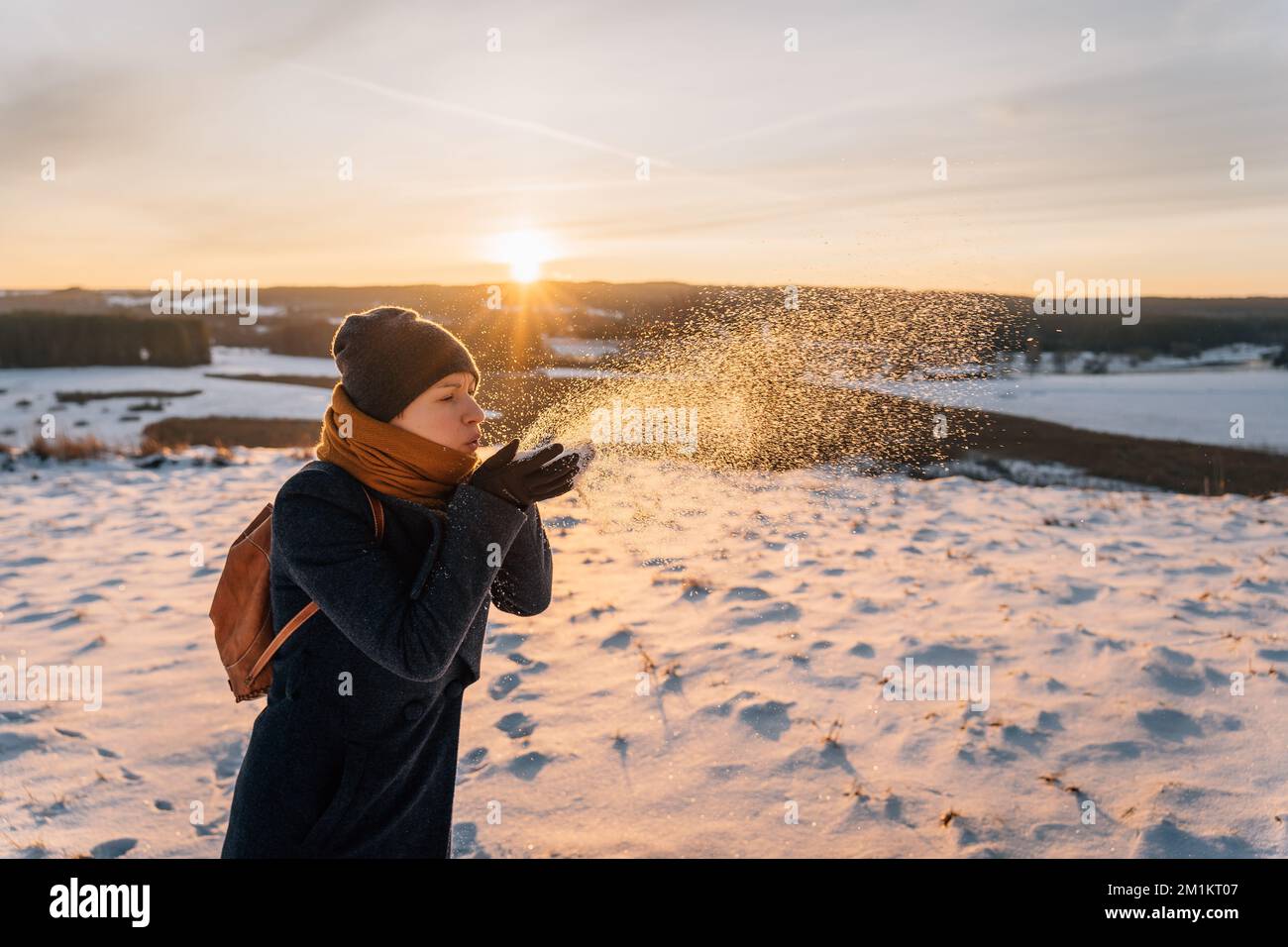 A woman on a snow-covered winter field blows snow off her palms Stock Photo