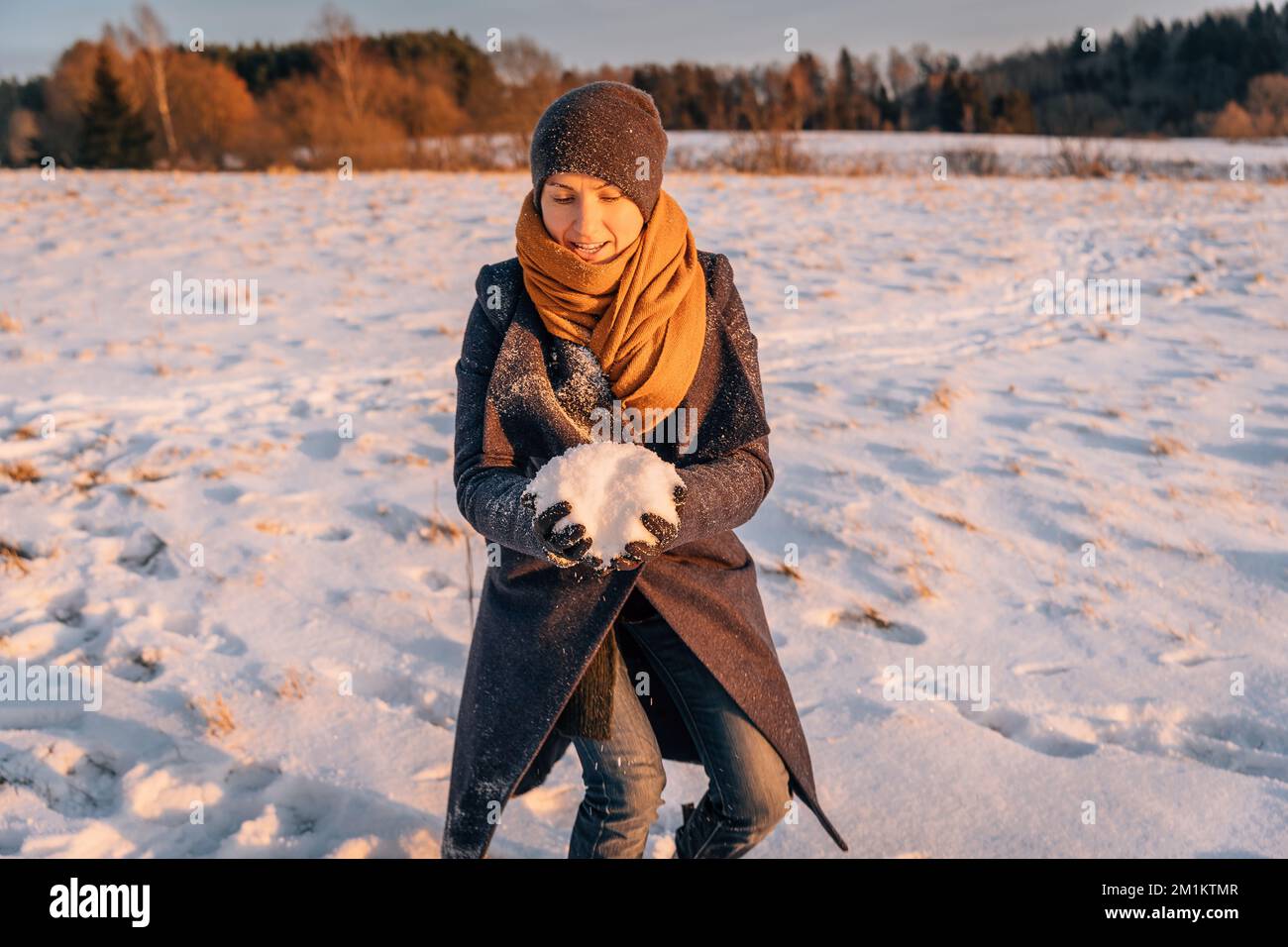 A woman in winter clothes collects a lump of snow in a snow-covered field Stock Photo