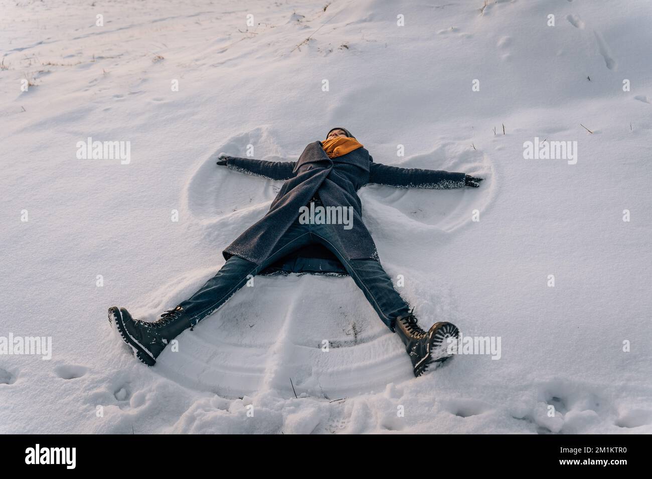 A young woman makes a snow angel lying in the snow with her arms and legs spread to the sides Stock Photo