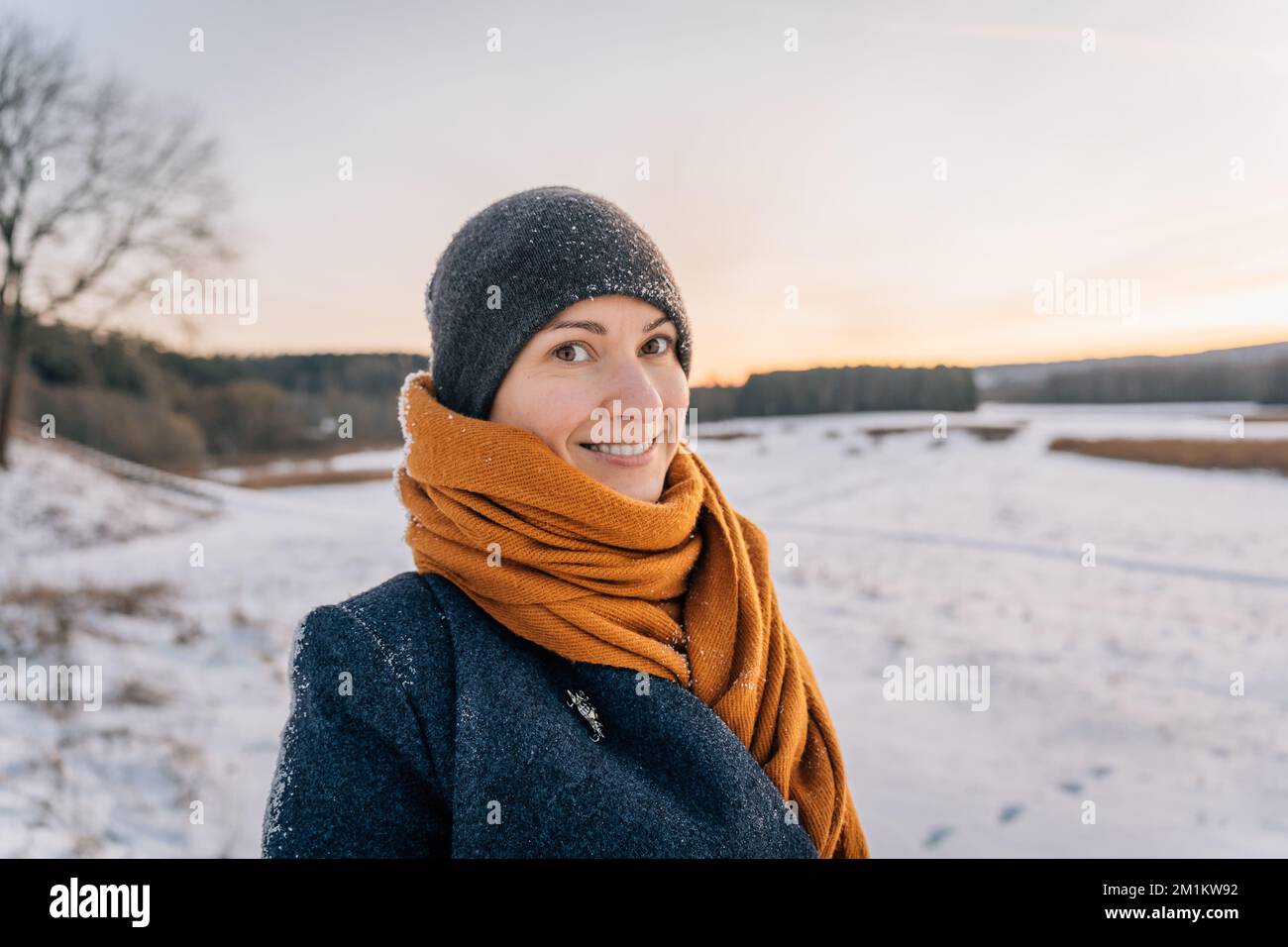 Portrait of a young woman in winter clothes and a hat wrapped in a scarf with a big smile Stock Photo