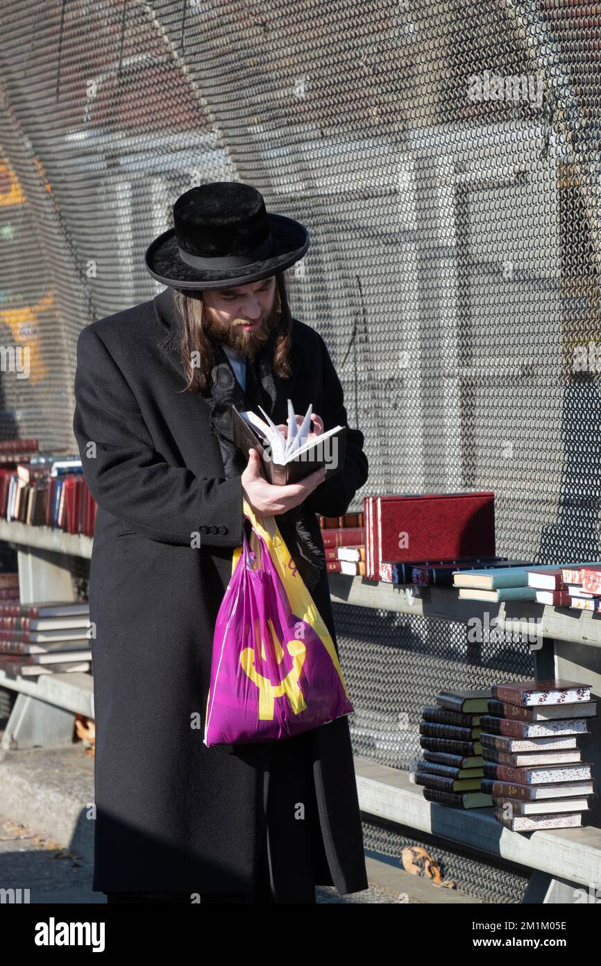 A young hasidic Jew with long peyot browses a religious volume at an outdoor book sale in Brooklyn, New York. Stock Photo