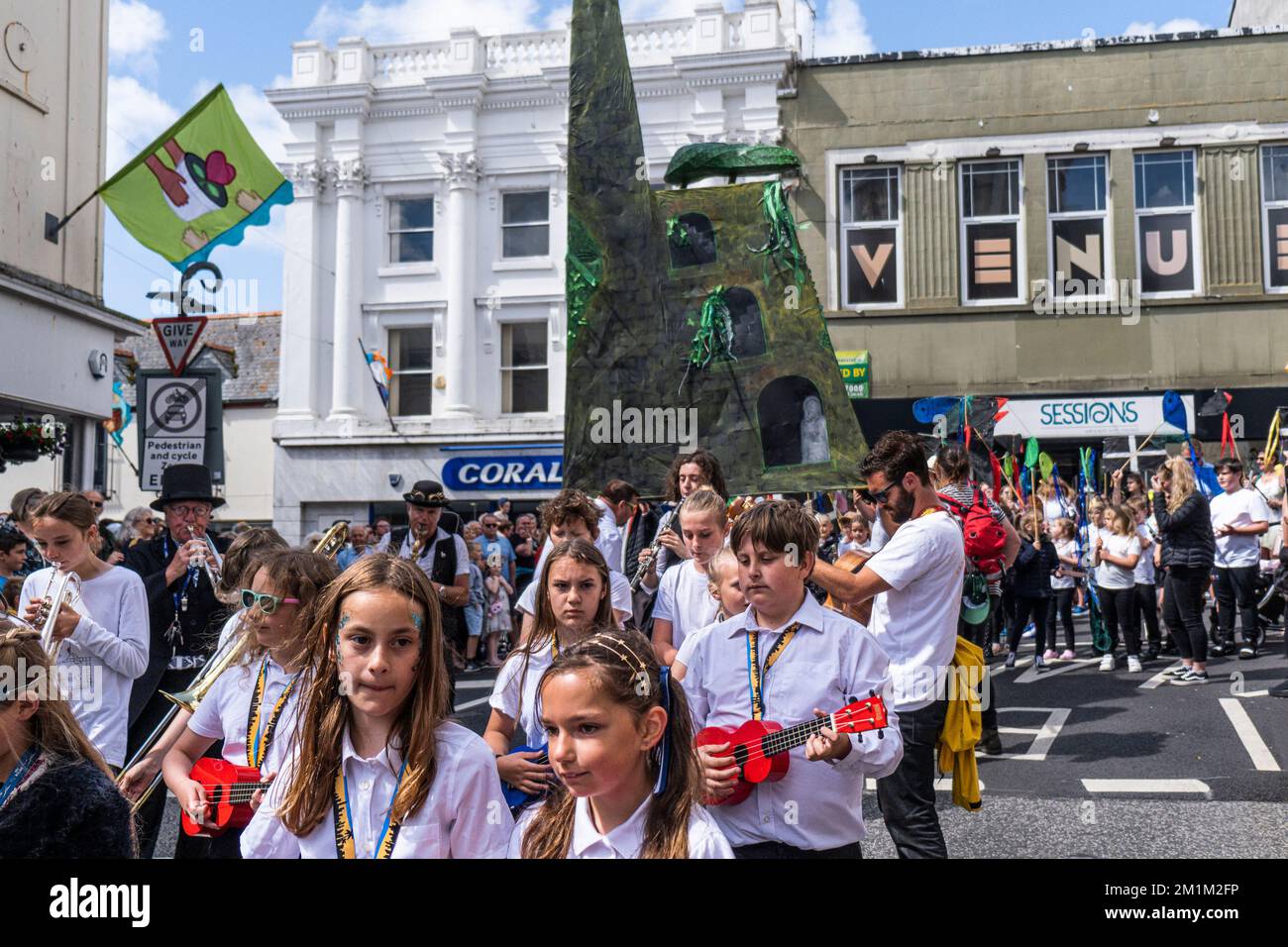 Adults and school children from Newlyn School playing instruments parading with their huge sculpture of a Cornish tin mine through Penazance on the co Stock Photo