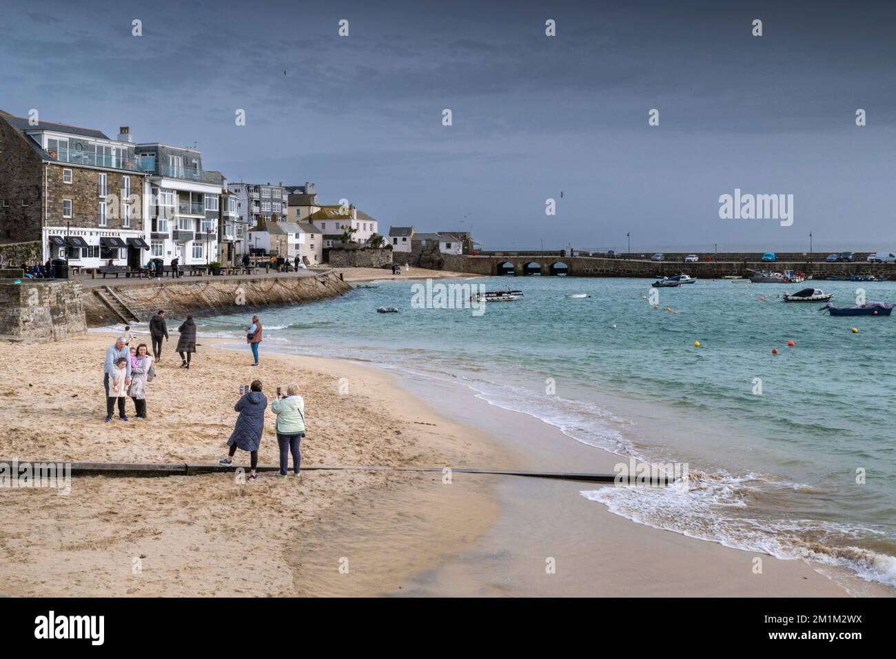 UK weather. Visitors on the beach on a rainy chilly miserable day in the historic seaside town of St Ives in Cornwall in England in the UK. Stock Photo