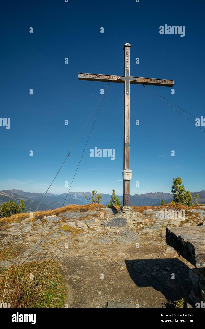 Wooden cross on the top of Gerlosstein in Austrian Alps with mountain panorama in the back on a sunny day of autumn with blue sky above. Mountain top Stock Photo