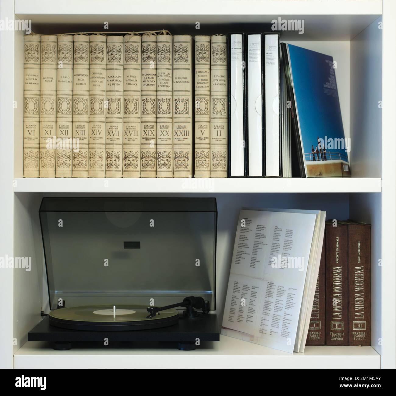 Two white shelves with a modern black turntable playing a translucent vinyl record and a varied collection of old and new vinyl records. Stock Photo