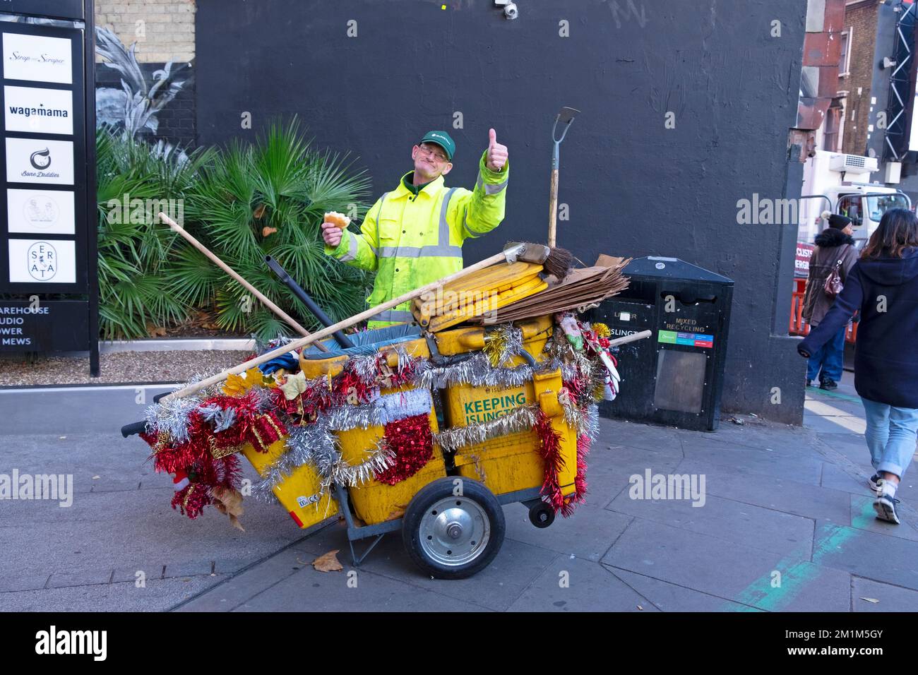 Dustman man worker street cleaner with Christmas decorations on his dustcart in Islington London England UK December 2022 Great Britain  KATHY DEWITT Stock Photo