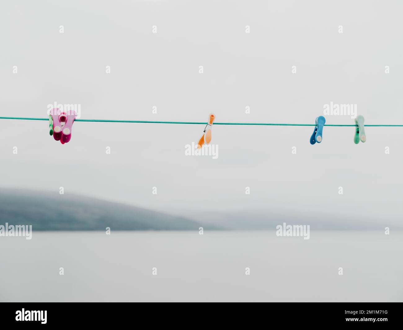 A green washing line with coloured plastic clothes pegs empty with a grey sky and sea background - clothes line, washing line, laundry line, seascape Stock Photo