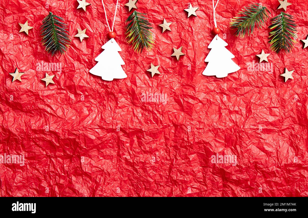 Red crumpled silk paper background with Christmas decorations on upper section, lot of copy space. Studio shot. White Christmas tree shape ornaments. Stock Photo