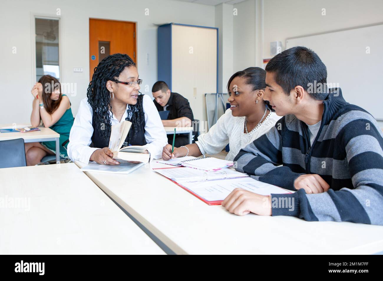 College Class: Teacher with Students. A pair of late teenage students working with their teacher in the classroom. From a series of related images. Stock Photo