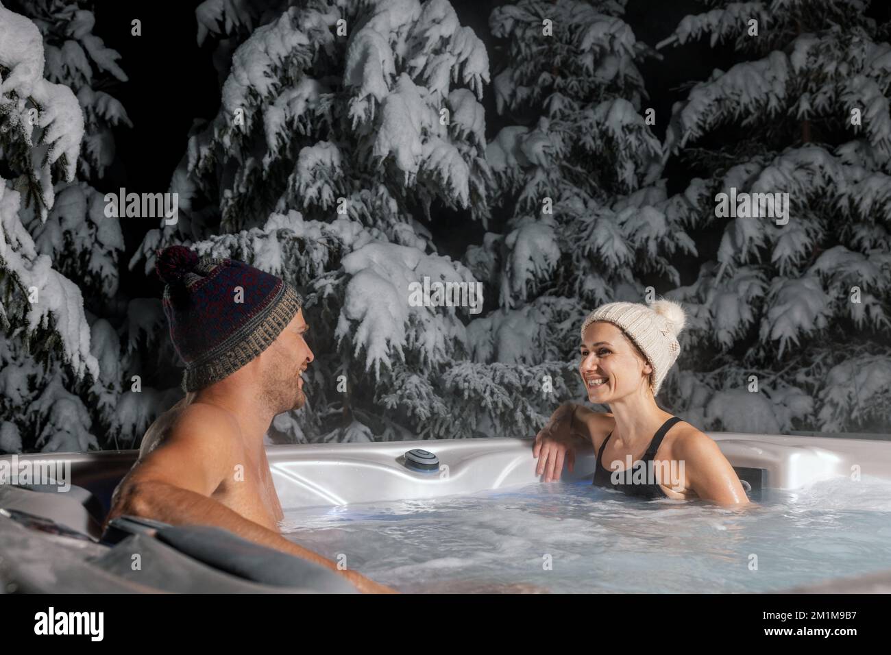 happy couple relaxing in outdoor hot tub at winter with snowy trees in background. spa resort Stock Photo