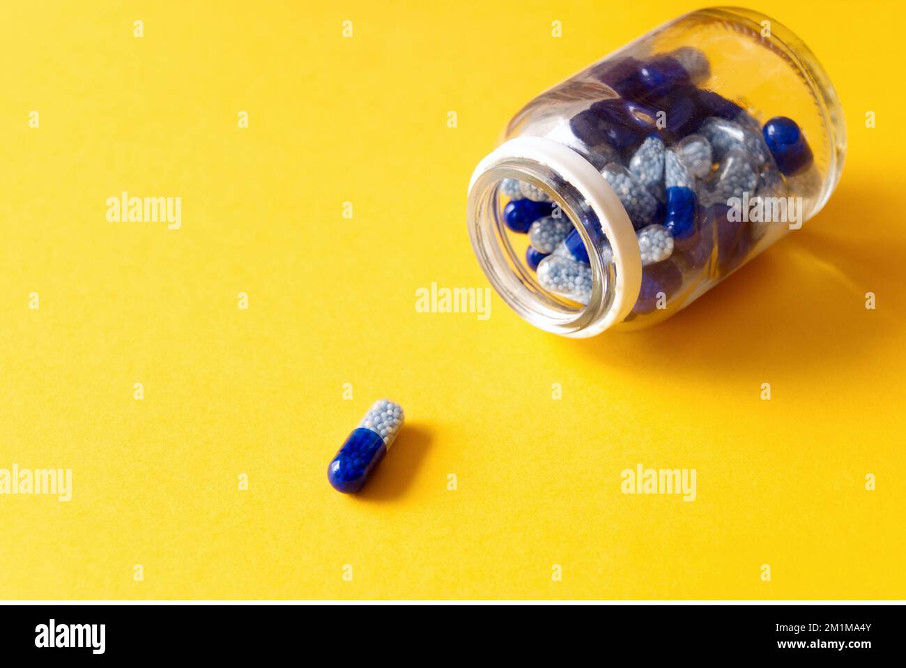 blue vitamin capsules spilled out of jar on yellow background Stock