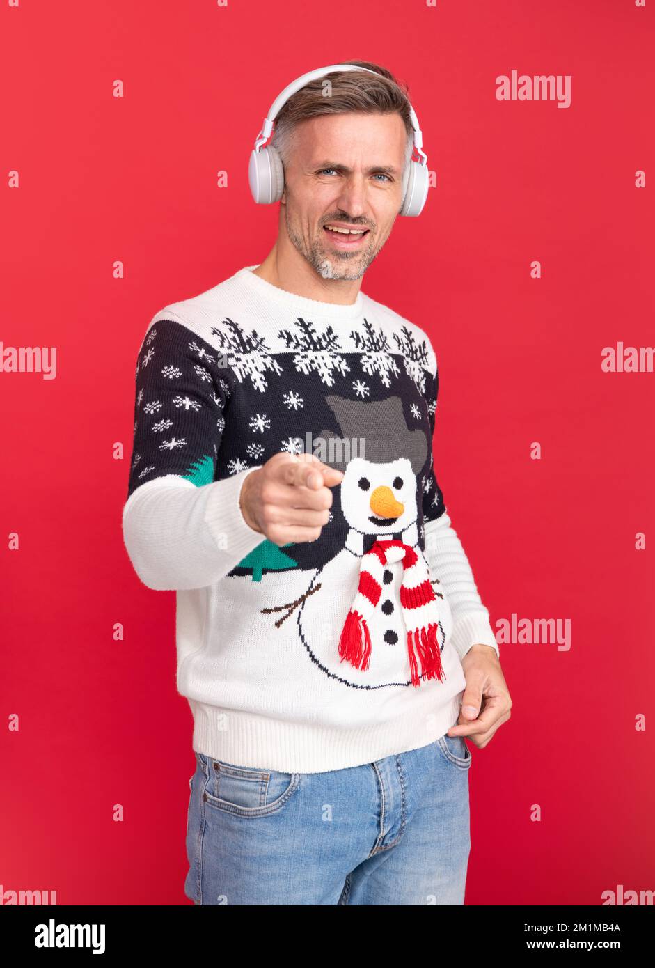 Christmas songs, man with headphone. Man in Christmas sweater and Santa hat on red background. Stock Photo