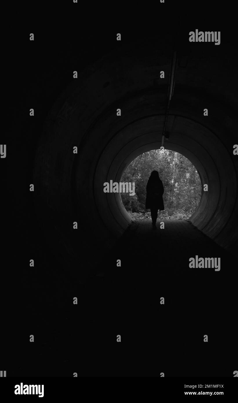 Silhouette of a girl walking inside a dark tunnel Stock Photo