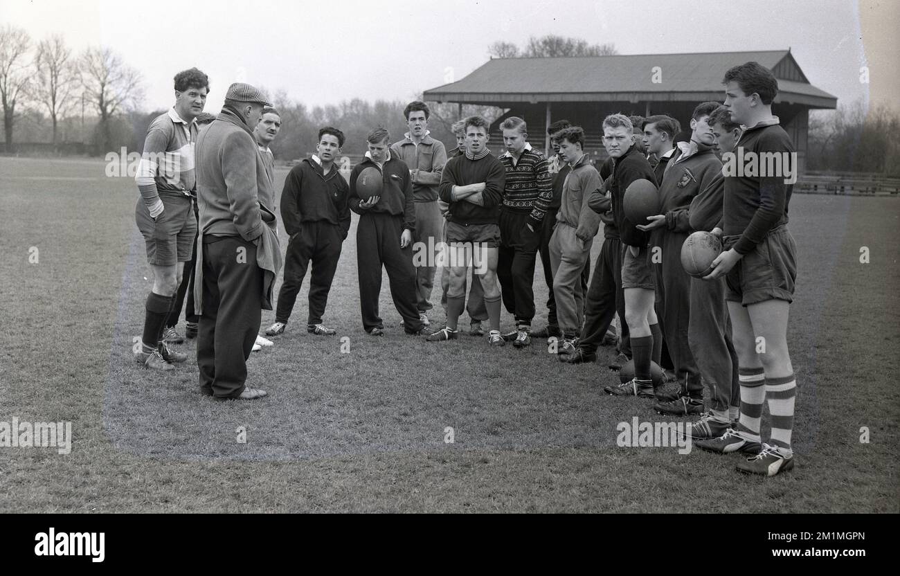 1950s, historical, members of the English Schools Rugby Football Union team at a training session outside on a pitch standing together getting instructions from one of the two adult male coaches in attendance, England, UK. All the boys are in the over 15 group, with some in shorts, but many wearing the baggy trousered cotton tracksuits of the era. Stock Photo