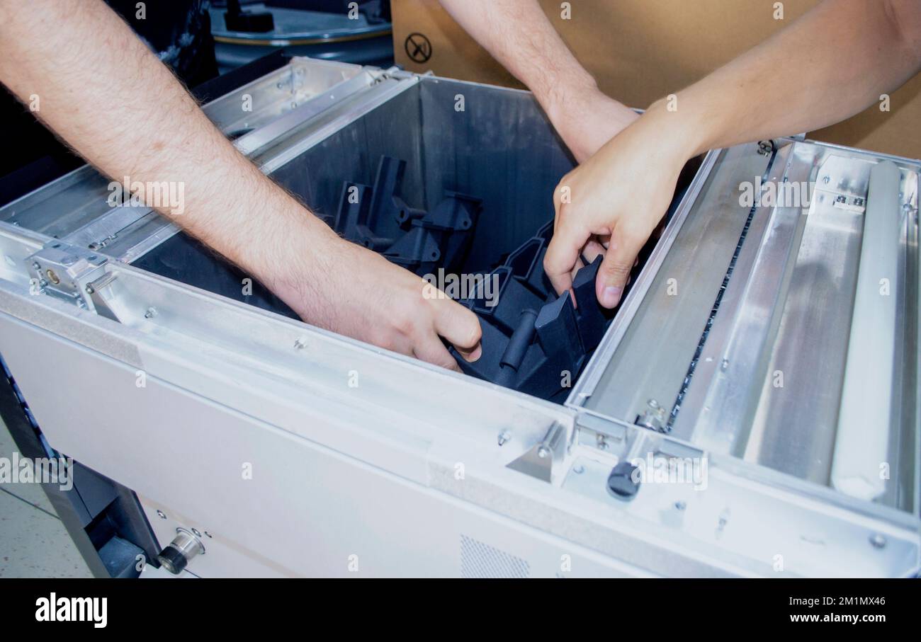 Man takes out model printed 3D printer from the workspace of a big industrial 3D printer. Model printed from polyamide powder. Two workers print an object on a powder 3D printer. Multi Jet Fusion Stock Photo