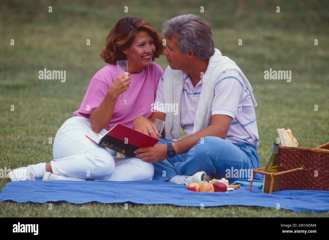 Middle aged couple outside having a picnic sitting on a blanket Stock Photo