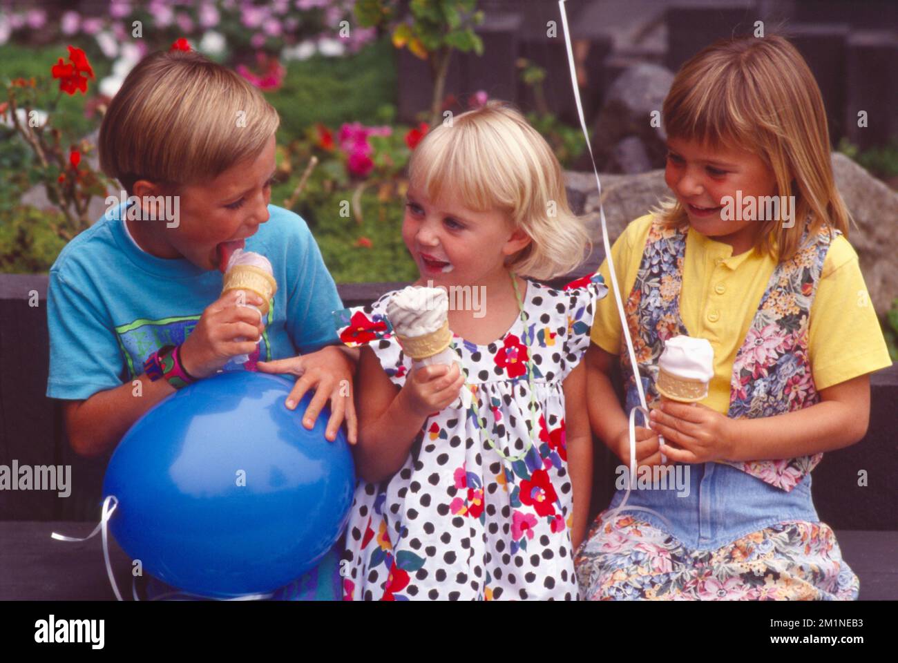 Boy and two girls sitting on a park bench eating ice cream Stock Photo