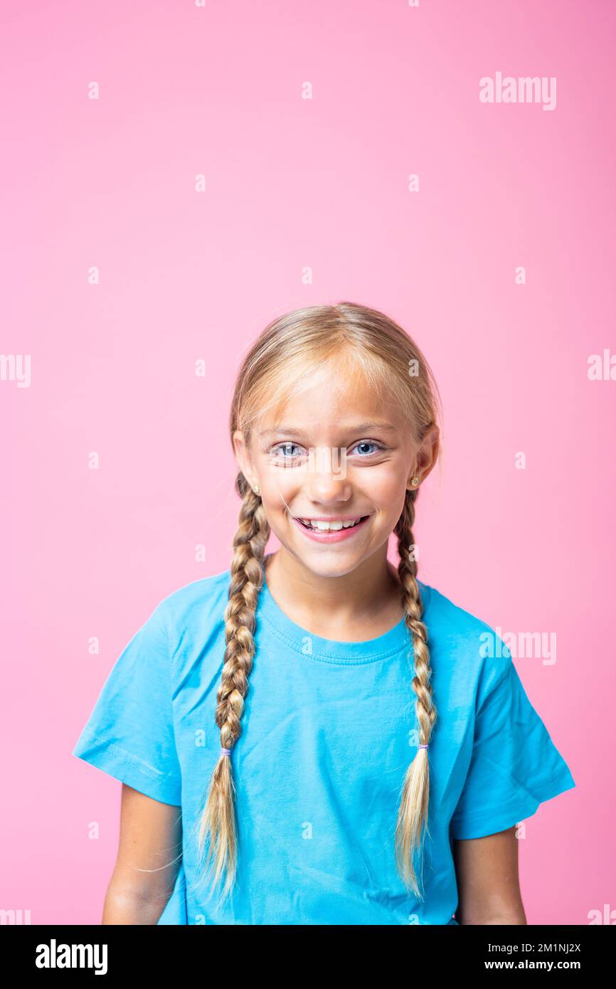 Vertical studio portrait with pink background of a happy little girl with braids Stock Photo