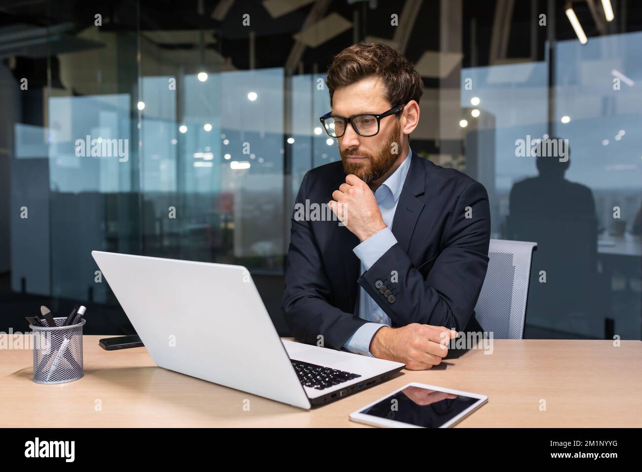 Work in the office of a financial analyst, banker, businessman. A young man sits at the table thoughtfully at a laptop. Stock Photo