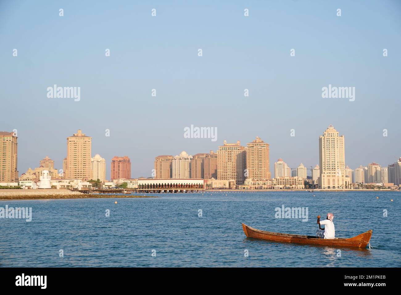 A local rowing a boat in front of the skyline at Katara Cultural ...
