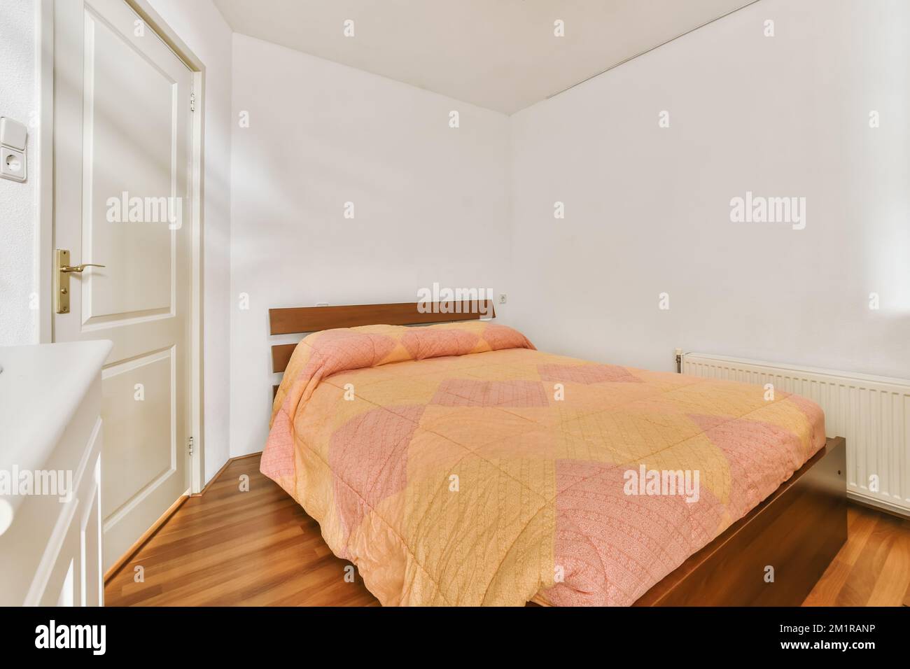 a bed in a room with wood flooring and white walls behind the bed is a