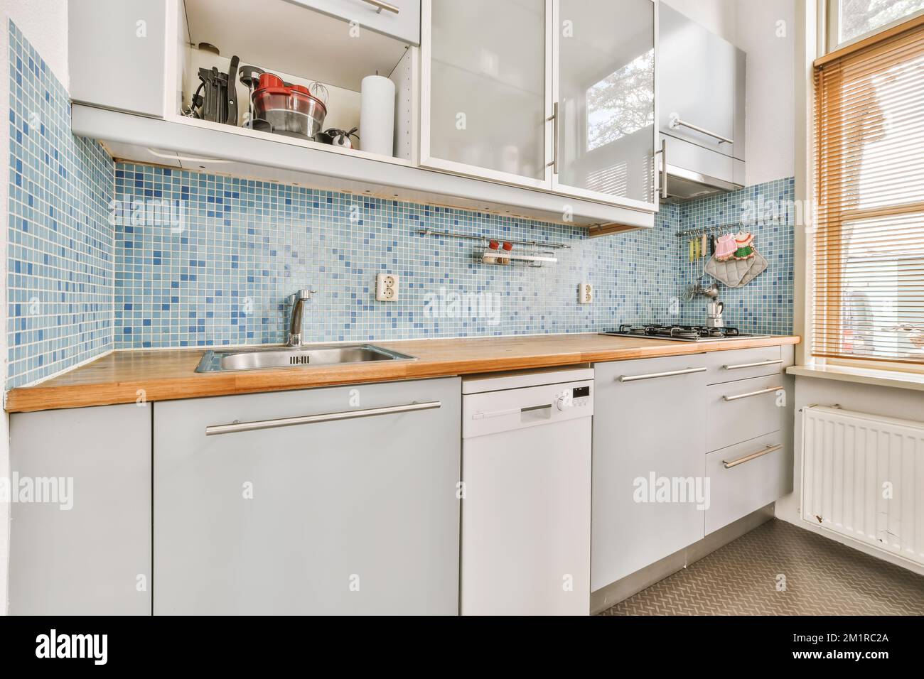 https://c8.alamy.com/comp/2M1RC2A/a-kitchen-with-white-cabinets-and-blue-tiles-on-the-wall-behind-it-is-an-oven-dishwasher-and-sink-2M1RC2A.jpg