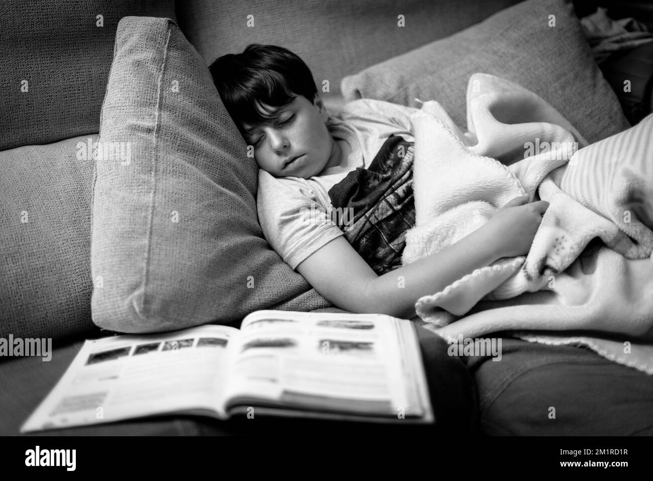 Child falls asleep on the sofa, while doing school reading homework