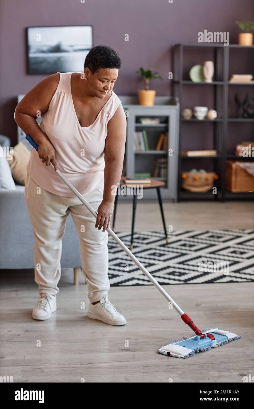 Vertical full length portrait of black senior woman mopping floors