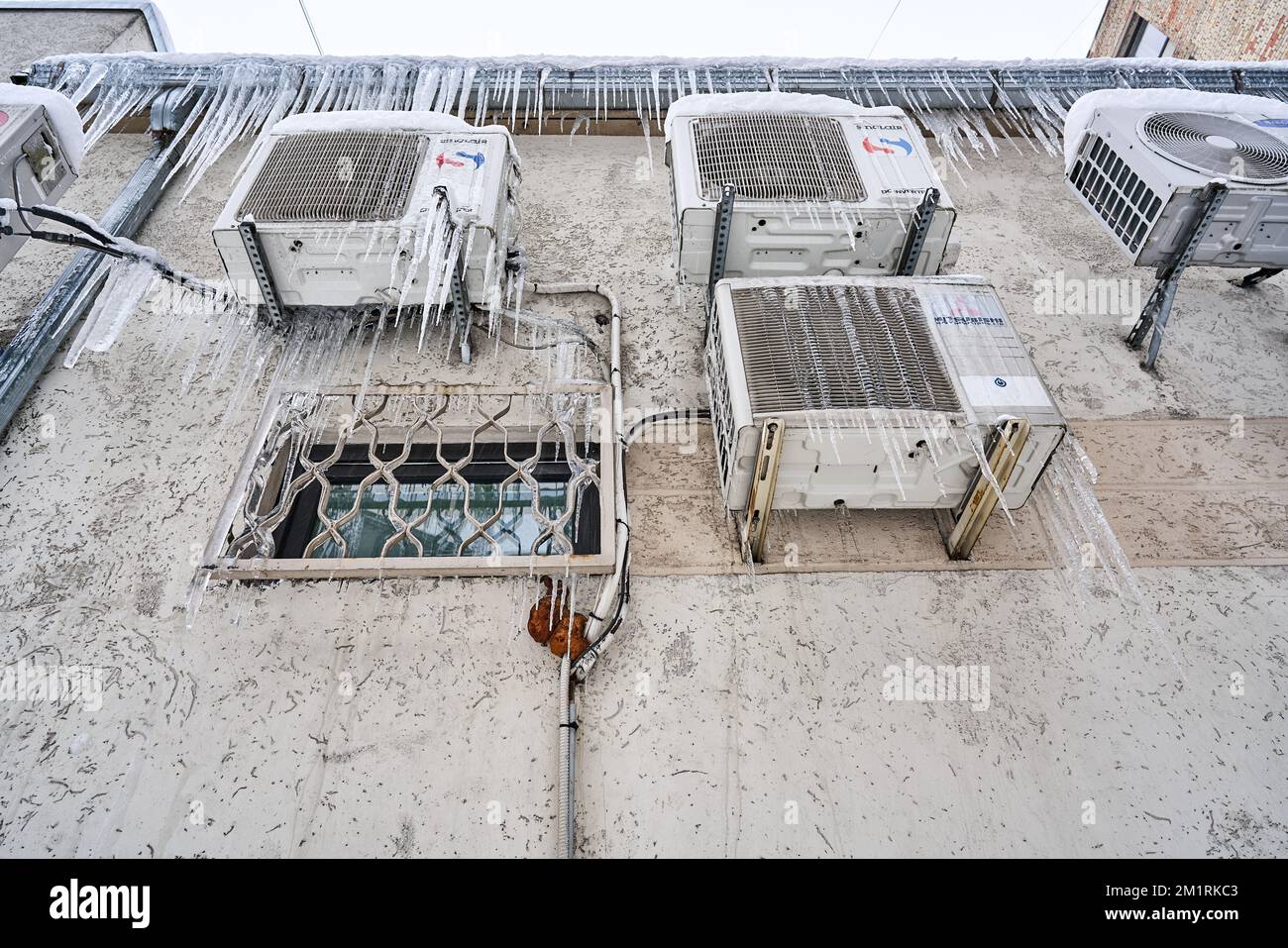 Riga, Latvia - 12 December, 2022: Various brands air conditioners mounted on the wall are frozen and covered in icicles. Bottom view. Stock Photo