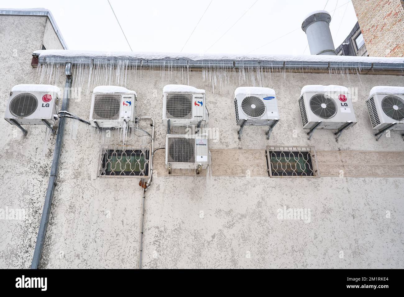 Riga, Latvia - 12 December, 2022: Various brands air conditioners mounted on the wall are frozen and covered in icicles. Stock Photo