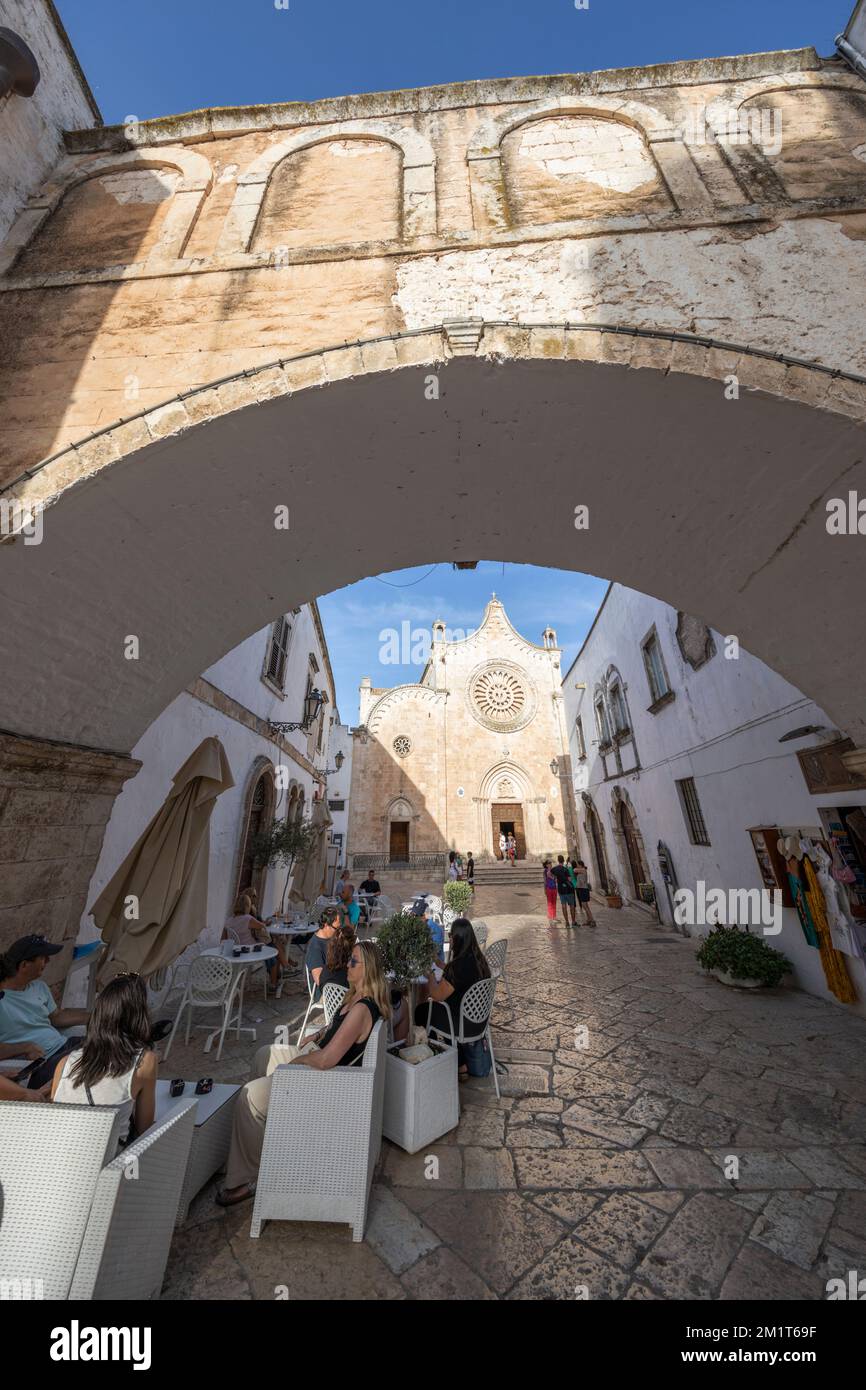 Cattedrale Santa Maria Assunta cathedral in the Largo Arcid Teodoro Trinchera square and cafe floodlit in evening framed by the Arco Scoppa in Ostuni Stock Photo